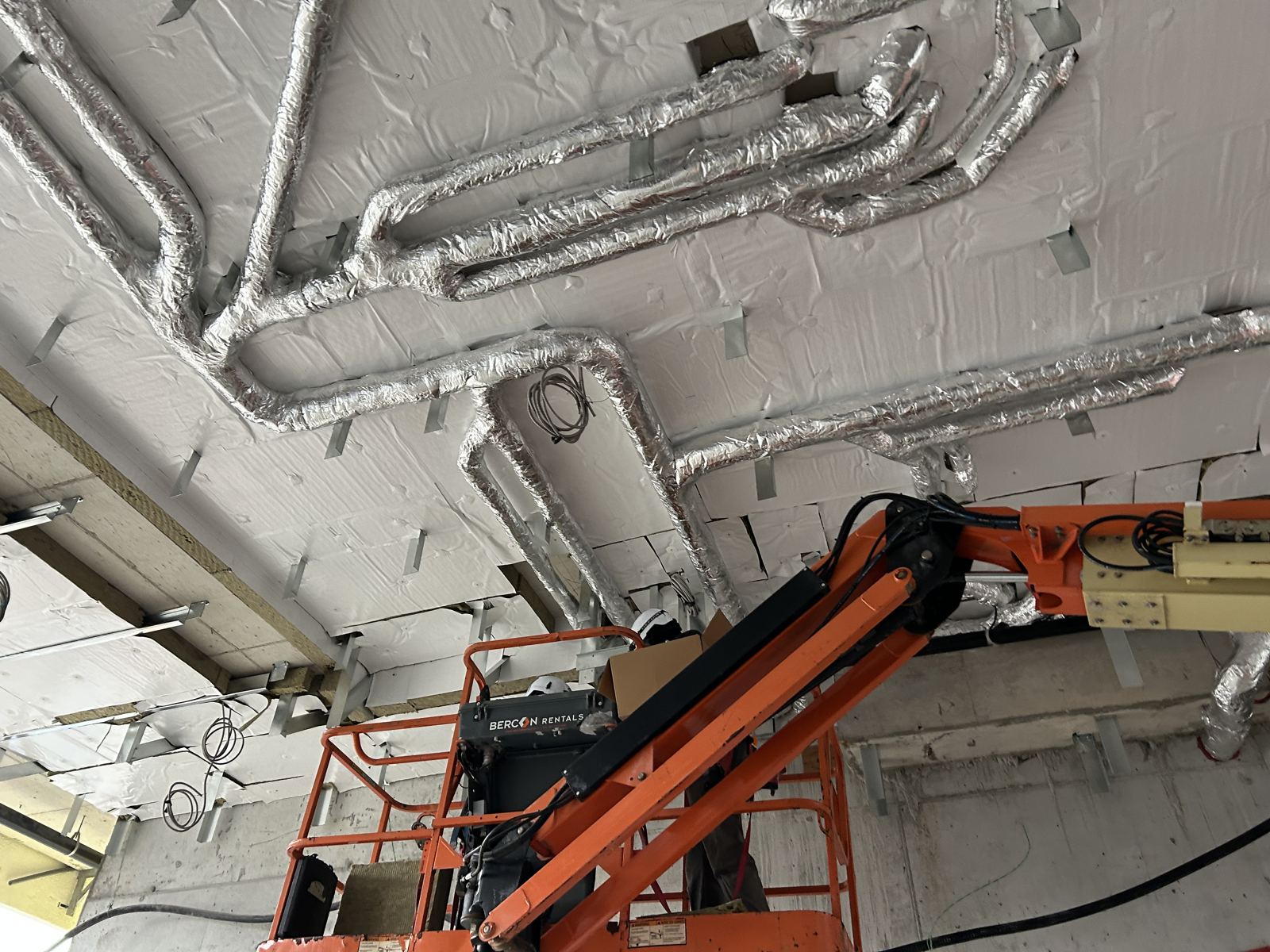 Foil-faced insulated pipe runs across a ceiling